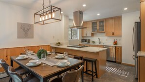 A modern kitchen with wooden cabinets, a central island, and a dining area with a table set for four. - Bernese Abode - Fireplace - Newly Updated! (Truckee)