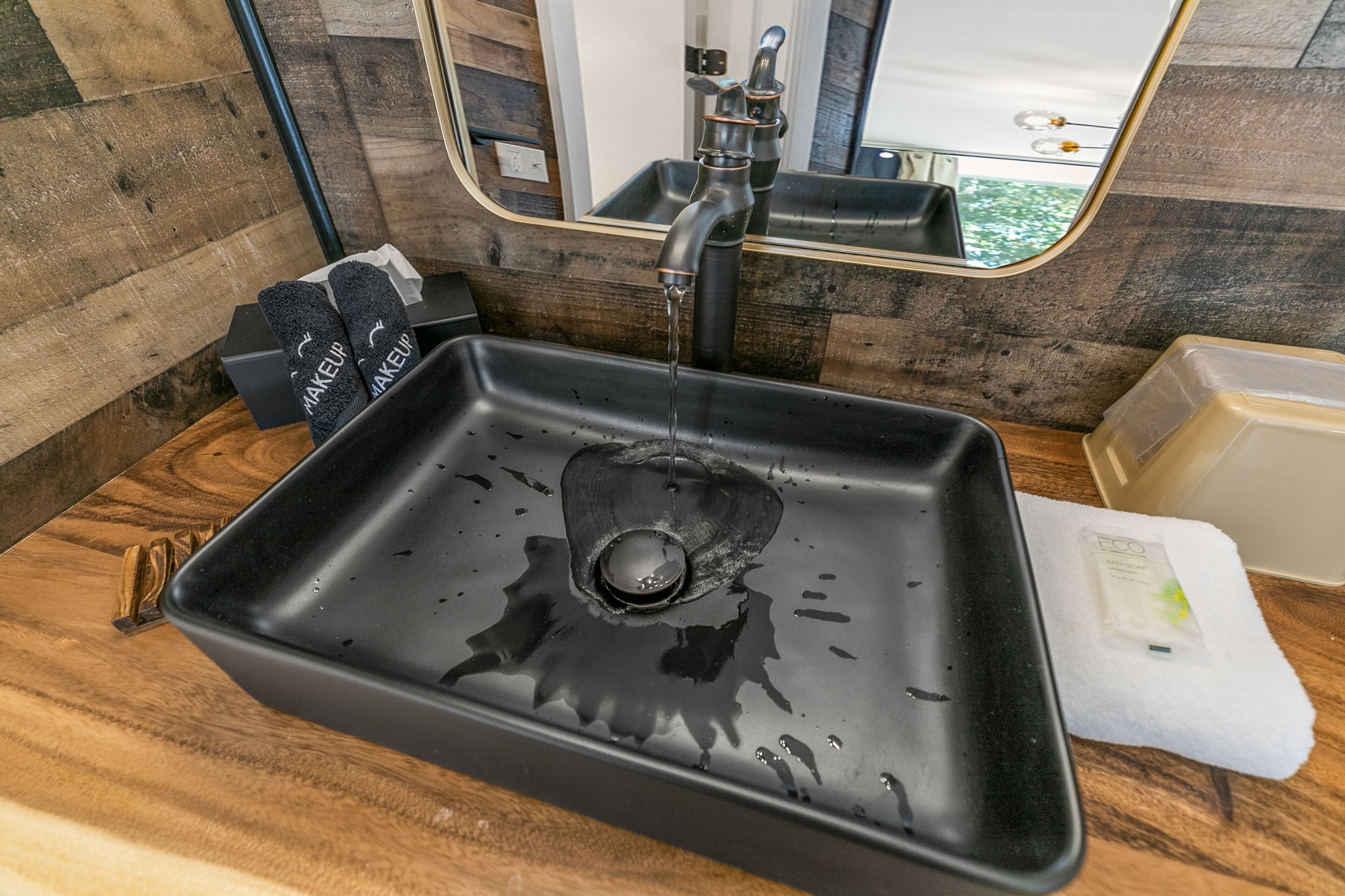 A black sink with water running, a mirror above it, and a wooden countertop.