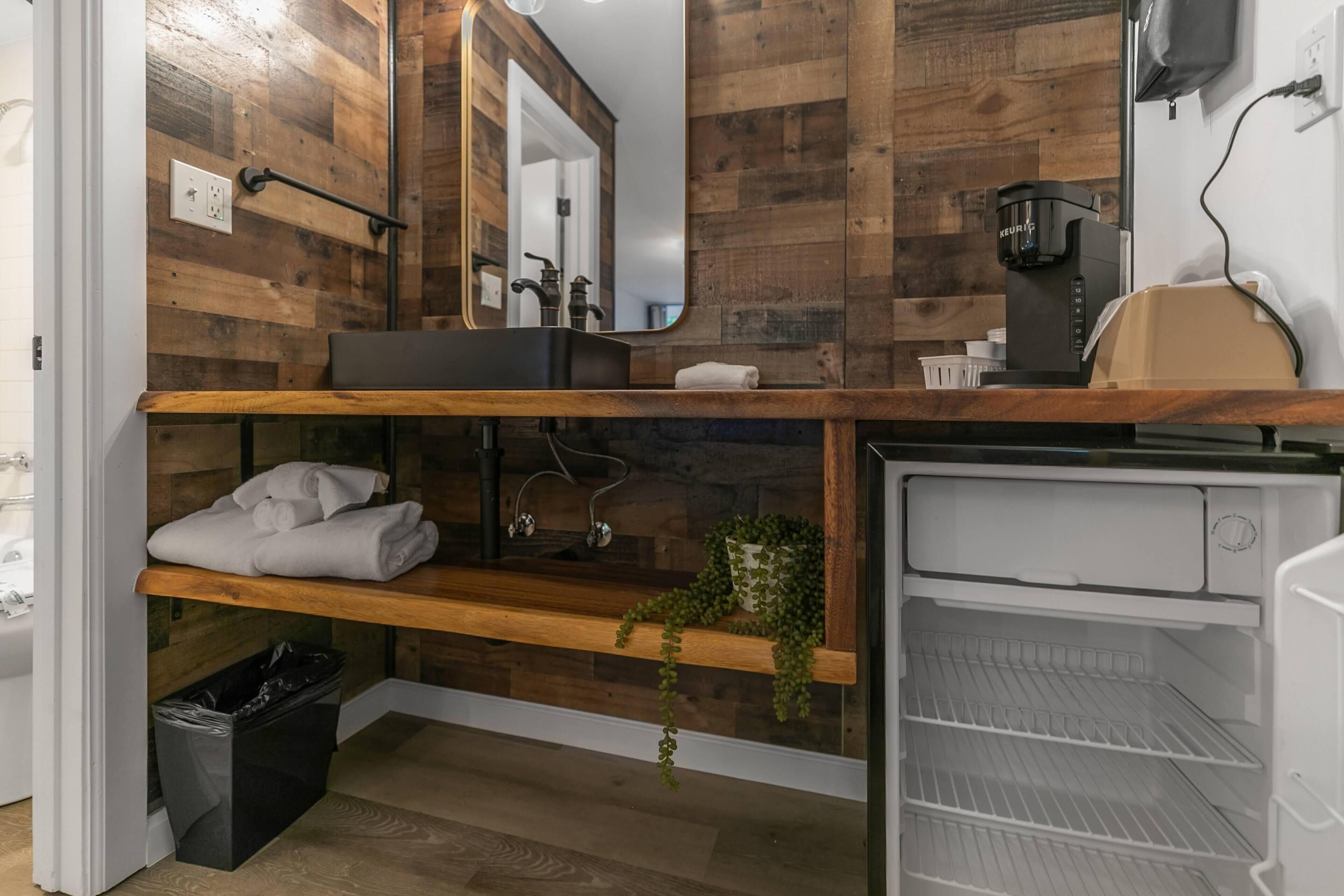 Een moderne badkamer met houten wanden, een inbouwwastafel, een spiegel, een koffieapparaat en een plank met handdoeken.