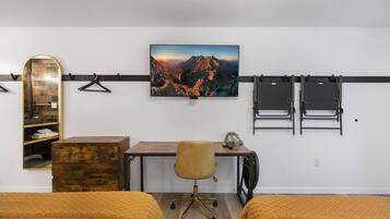 Une chambre avec deux lits, un bureau, une chaise, un miroir et un téléviseur fixé au mur qui diffuse un paysage de montagne.