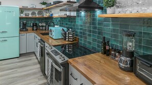 Una cocina moderna con mostradores de madera, horno integrado, estación de café y baldosas de resalte color turquesa.