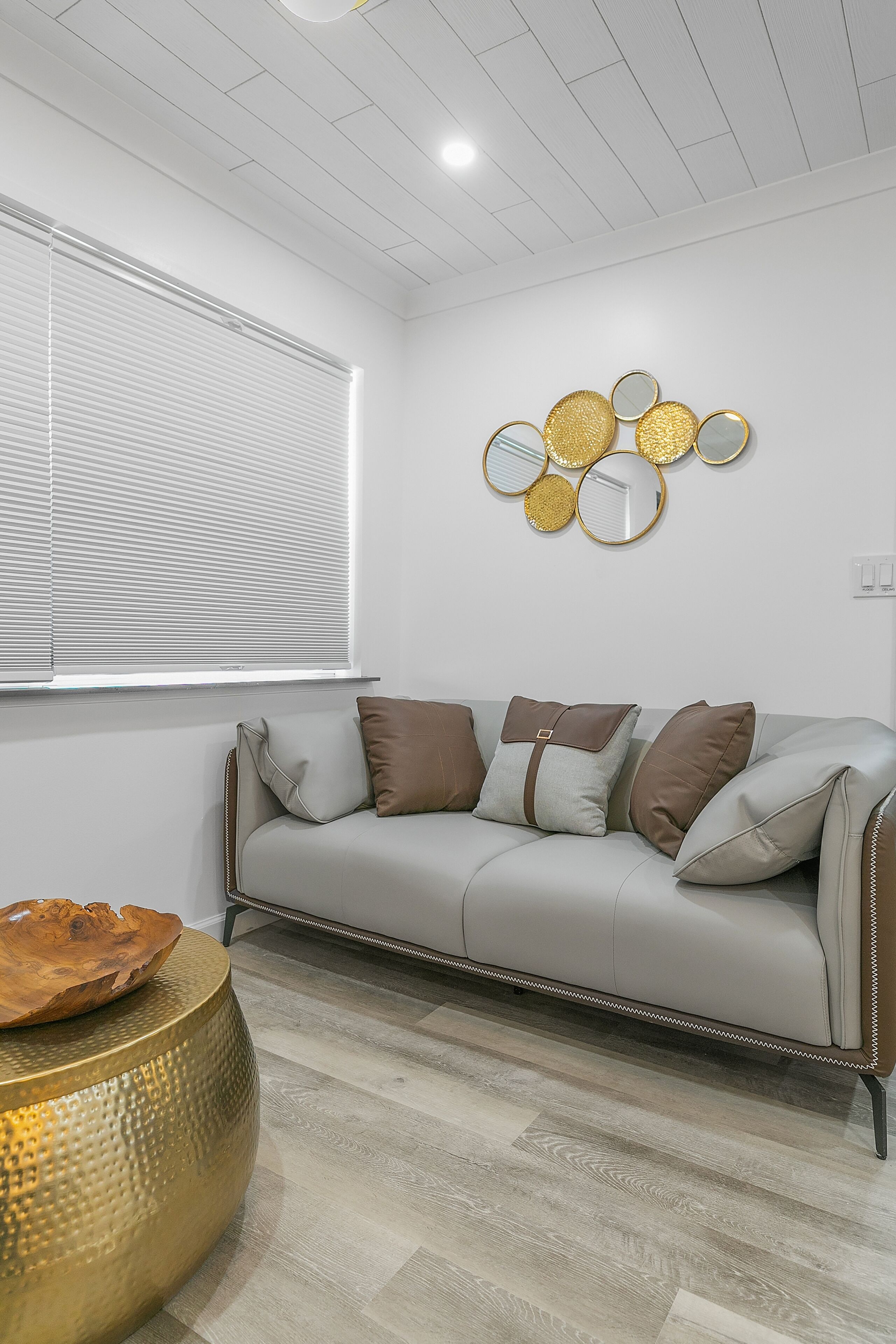 A modern living room with a grey sofa, a round gold side table, and a wall-mounted mirror arrangement.