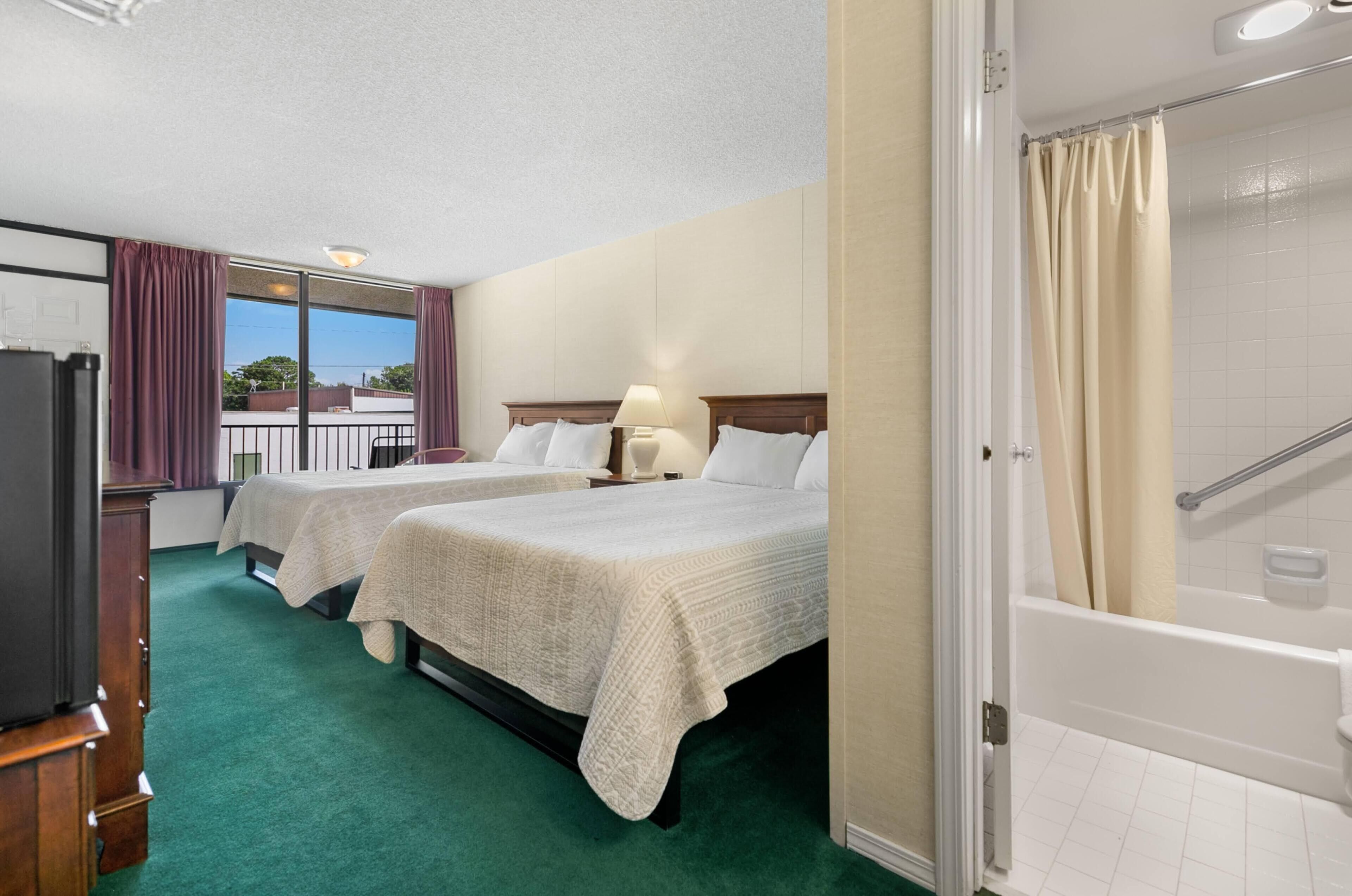 Une chambre d’hôtel avec deux lits, une salle de bain avec baignoire et vue sur l’extérieur.