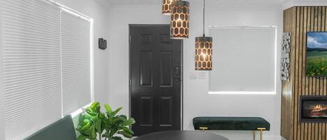 A modern interior with a green sofa, two round tables, pendant lights, a wooden wall panel, and a fireplace.