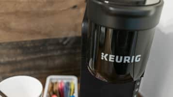 A Keurig coffee maker on a wooden surface with a paper cup and a container of coffee pods.