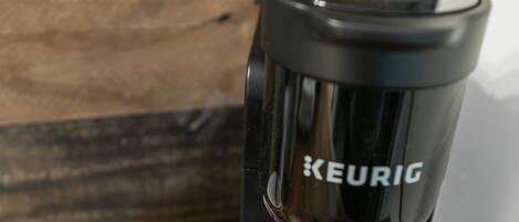 A Keurig coffee maker on a wooden surface with a paper cup and a container of coffee pods.