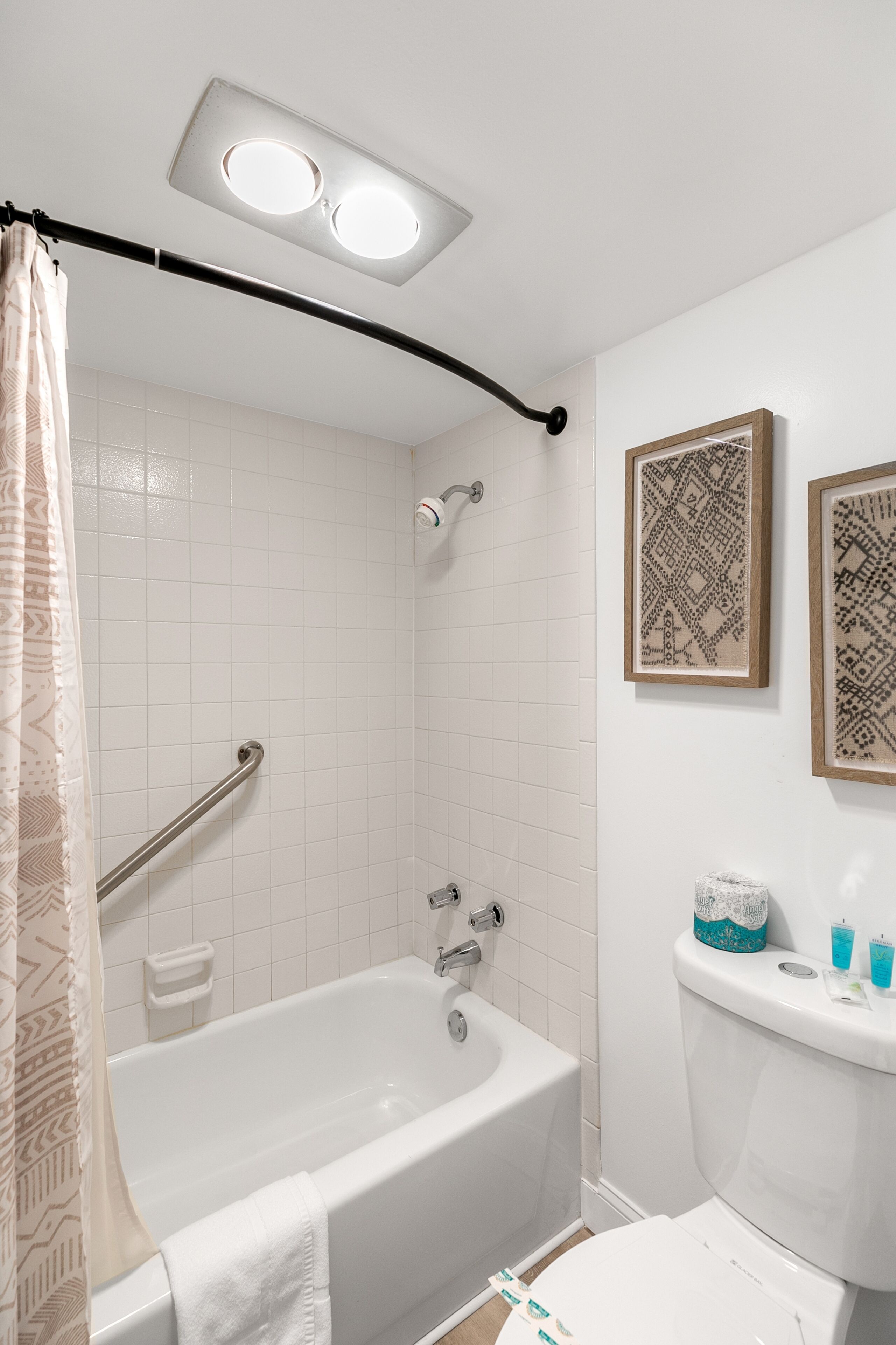 A bathroom with a bathtub, a shower, a toilet, and a handrail.