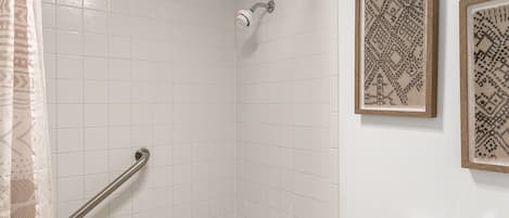 A bathroom with a bathtub, a shower, a toilet, and a handrail.