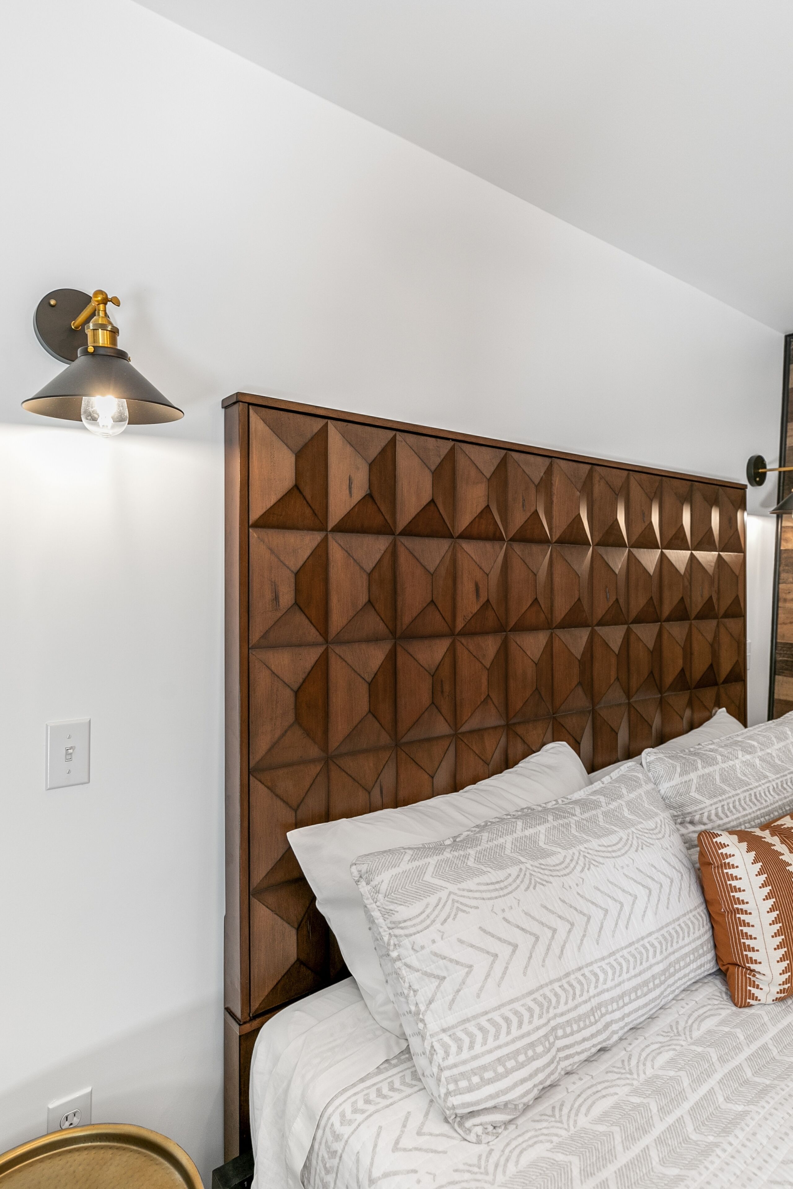 A bedroom with a geometric-patterned headboard, a bedside lamp, and patterned bedding.