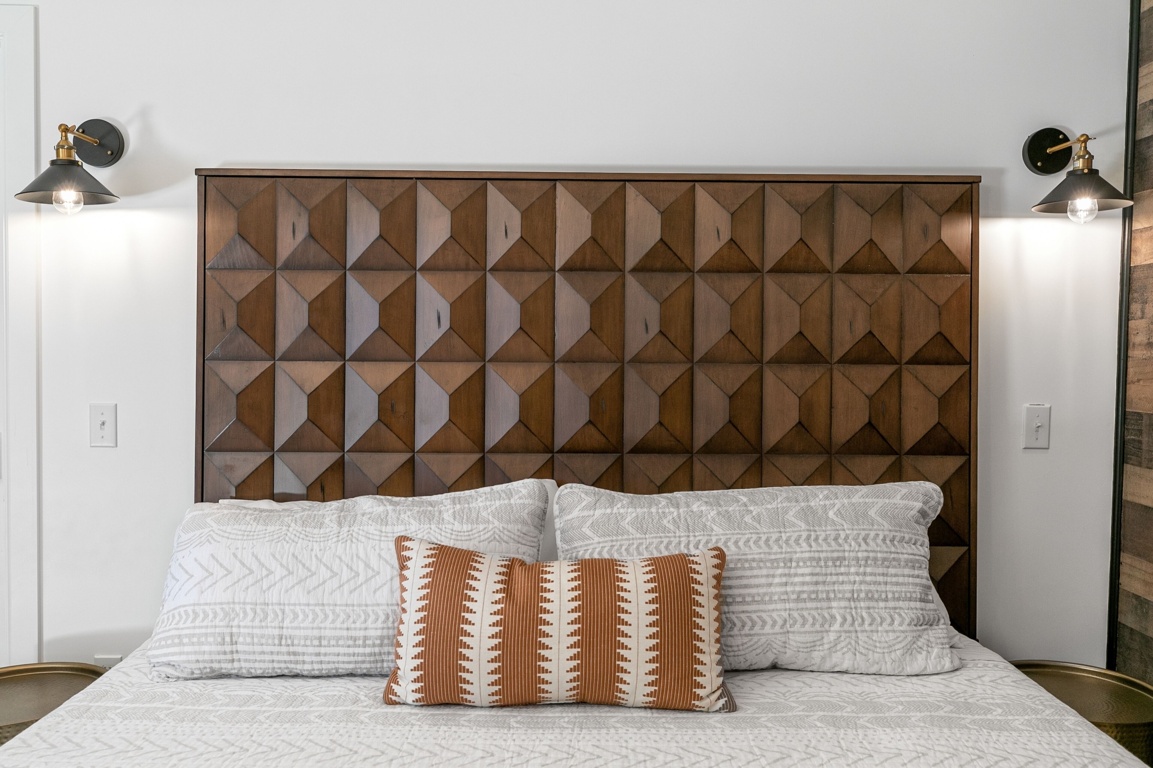 Une chambre à coucher avec une tête de lit à motifs géométriques, deux lampes de chevet et une literie à motifs.