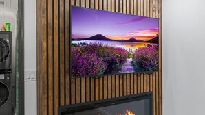 Una sala de estar moderna con un televisor de pantalla plana montado en una pared de paneles de madera, una chimenea abajo y un área de lavandería visible a la izquierda.