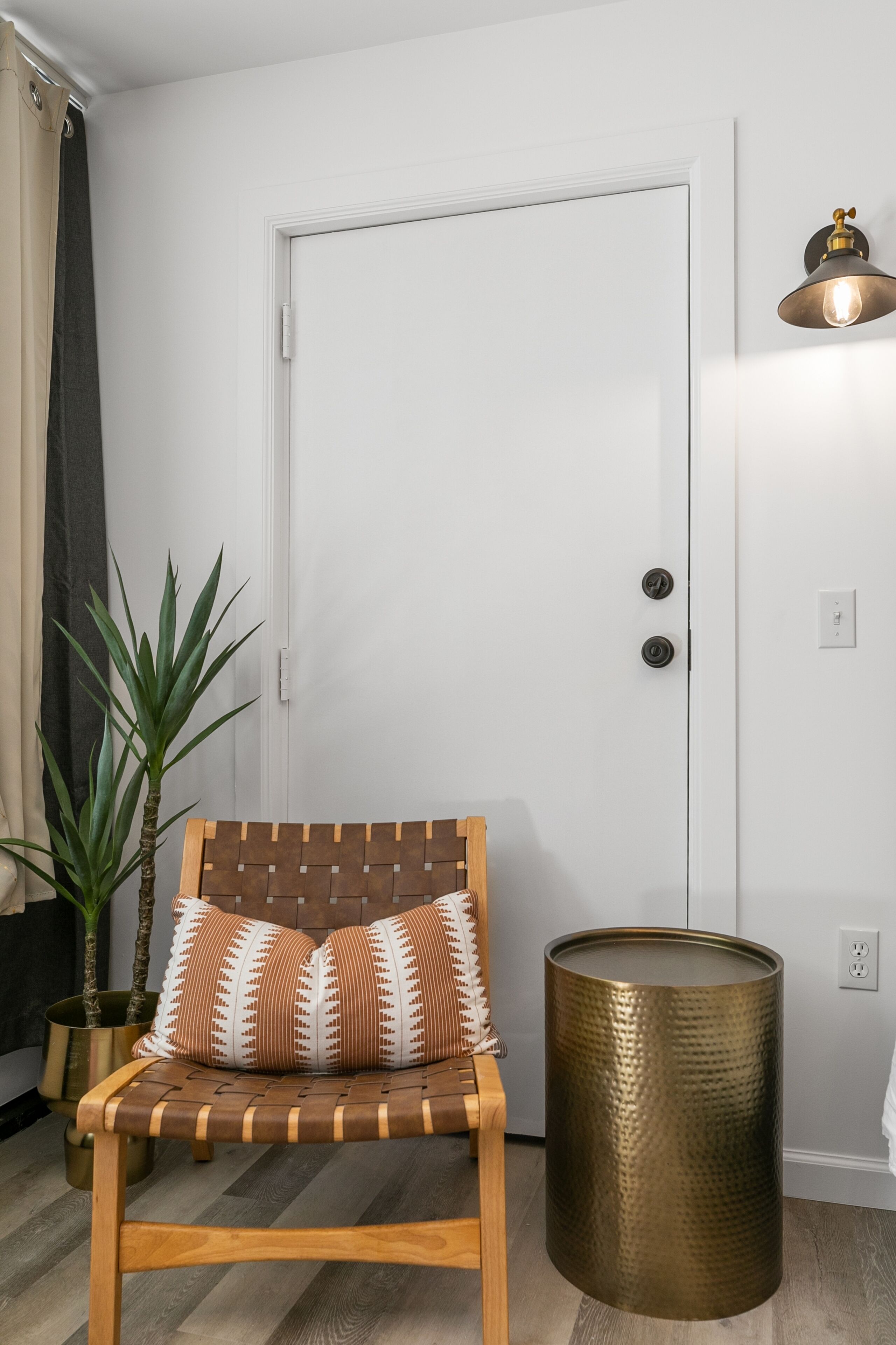 A room with a wooden chair with patterned cushions, a potted plant, and a brass-colored cylindrical object.