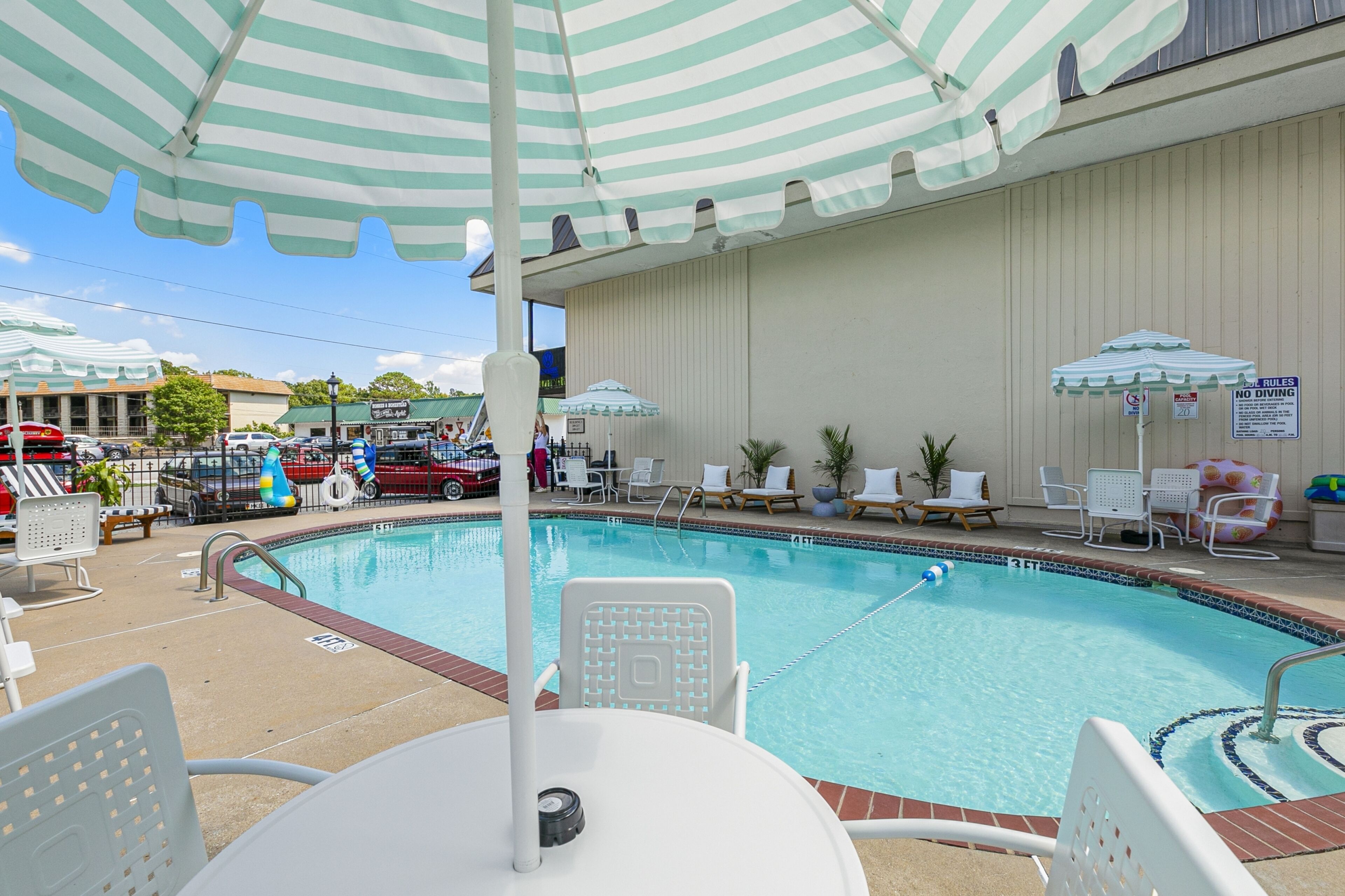 A swimming pool with lounge chairs and umbrellas, surrounded by a building with a tiled pool deck.