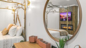 Un dormitorio moderno con un espejo redondo grande, una cama con sábanas blancas, un cabecero de madera y una mesita de noche con un reloj y una planta.