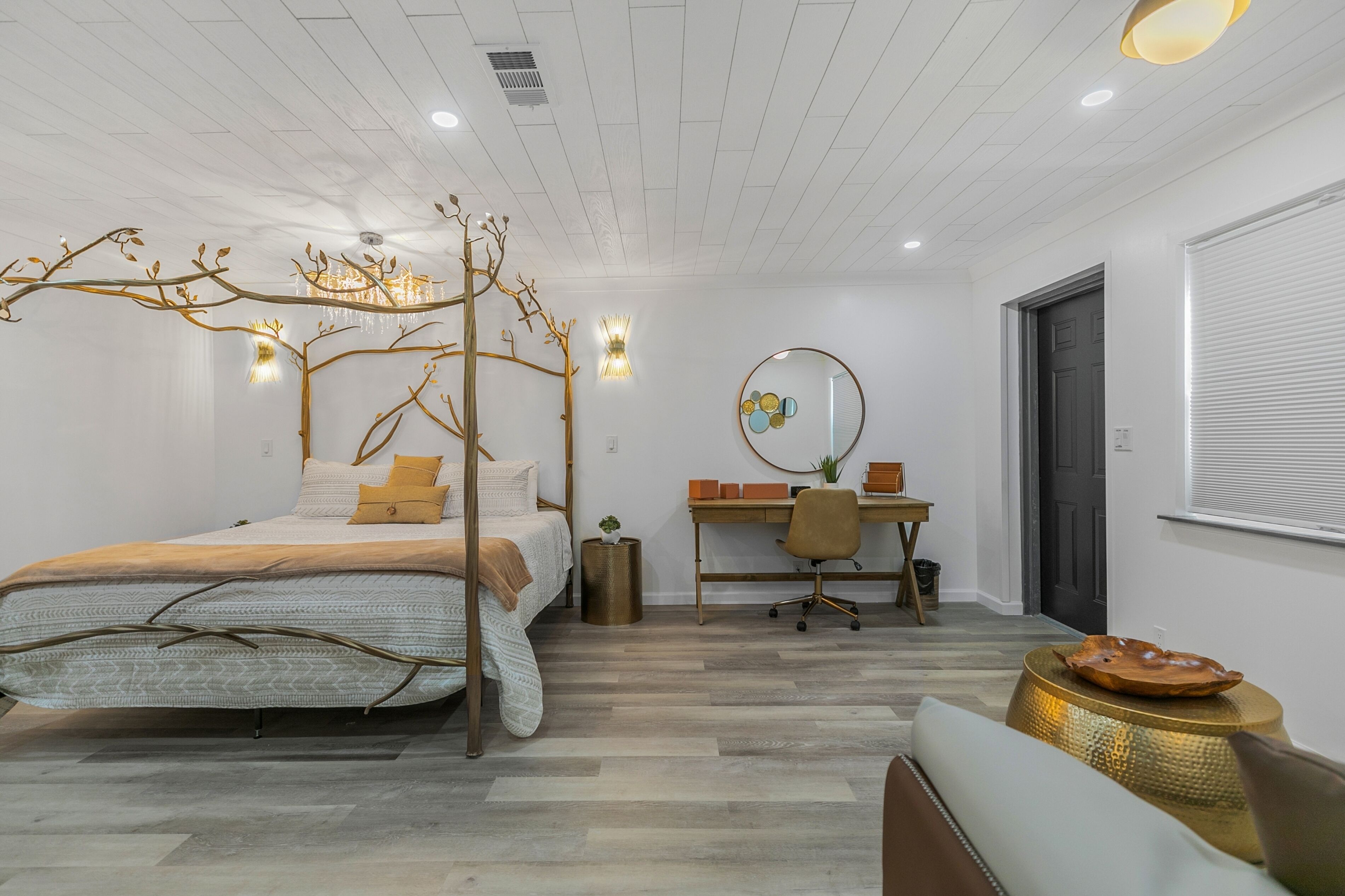 Une chambre à coucher moderne avec un lit à baldaquin, un bureau avec une chaise et un miroir rond accroché au mur.