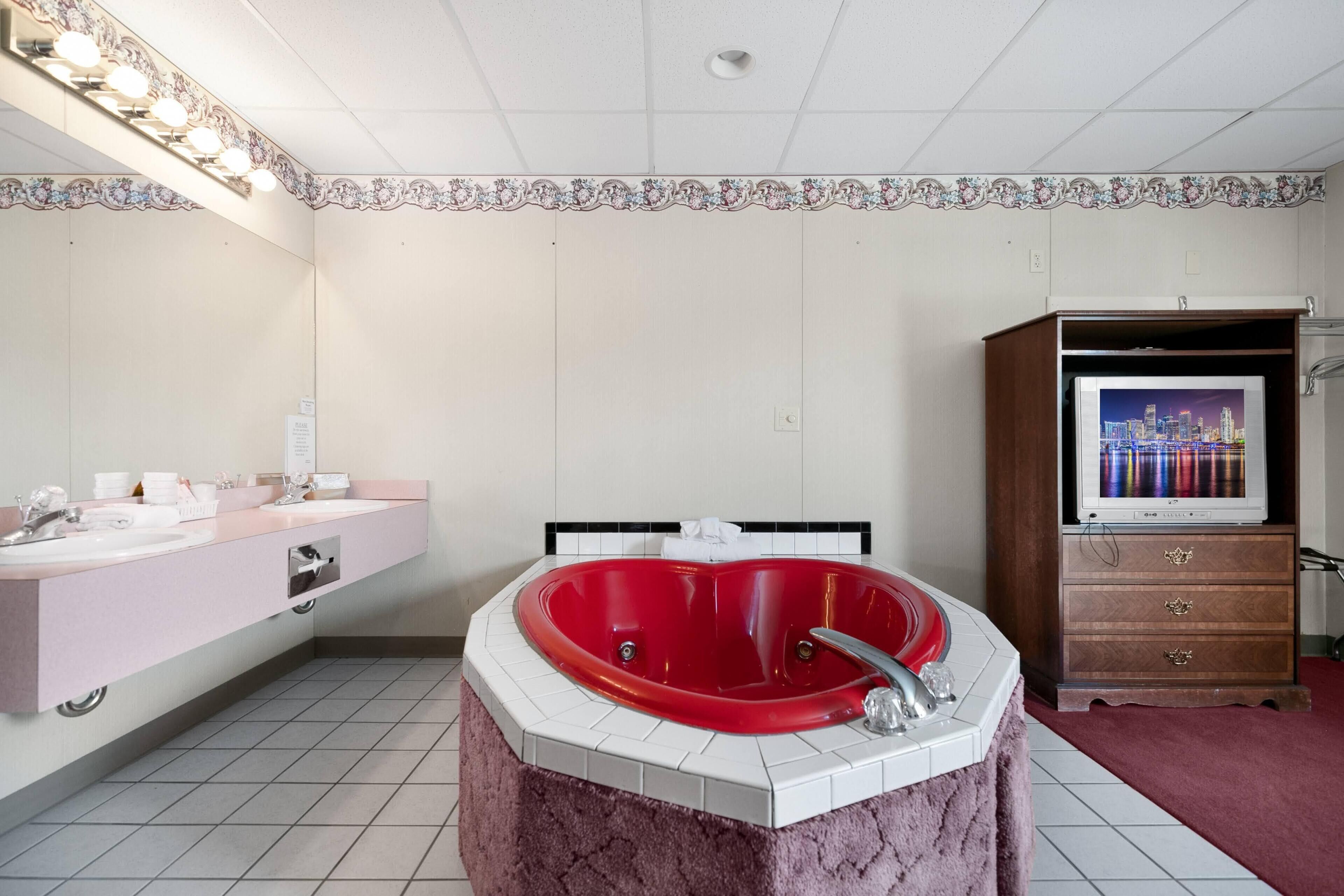 Un baño con una tina de hidromasaje roja, un tocador con espejo y un televisor sobre un mueble.