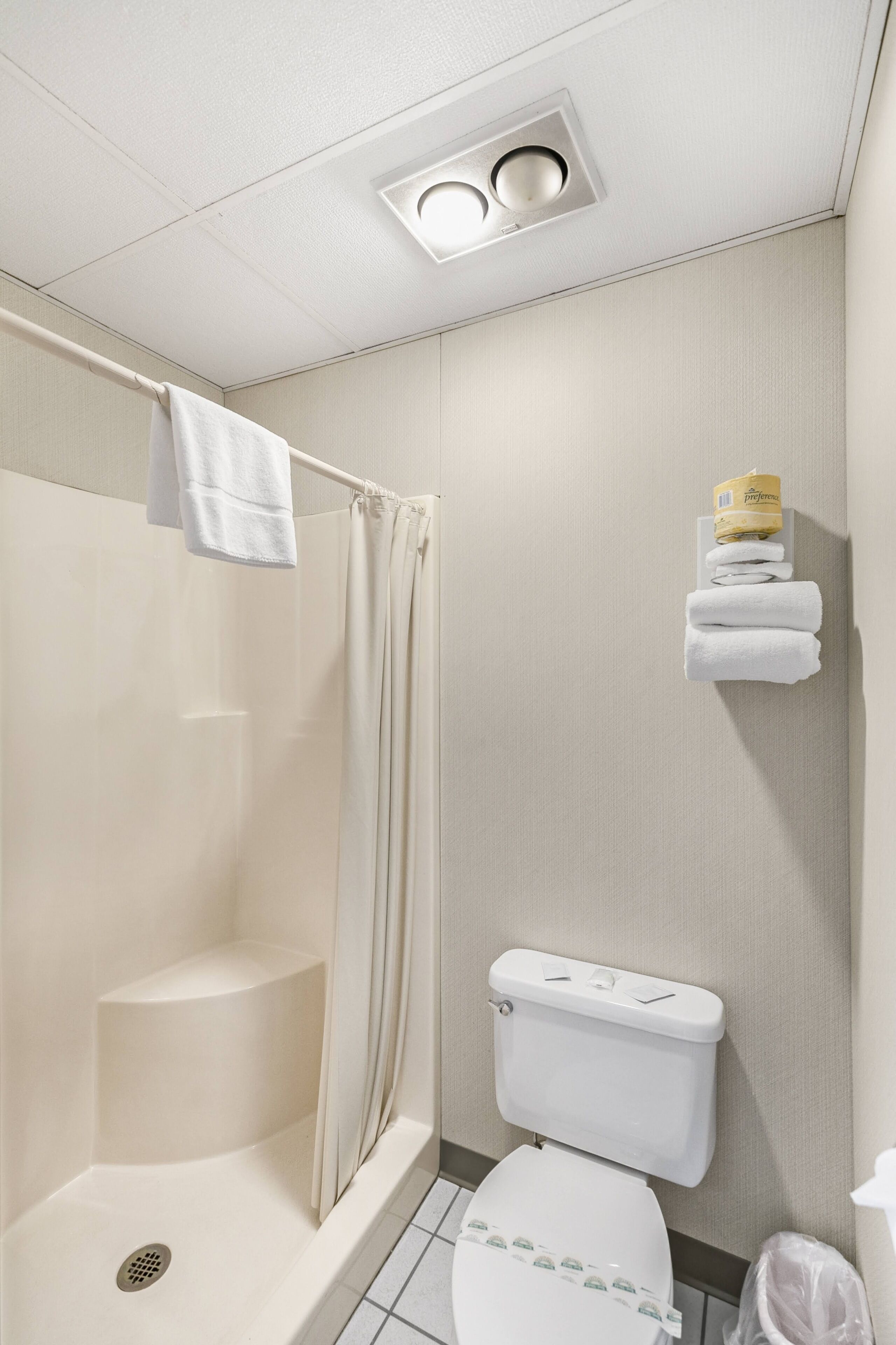 A bathroom with a shower, toilet, and a towel rack with folded towels.