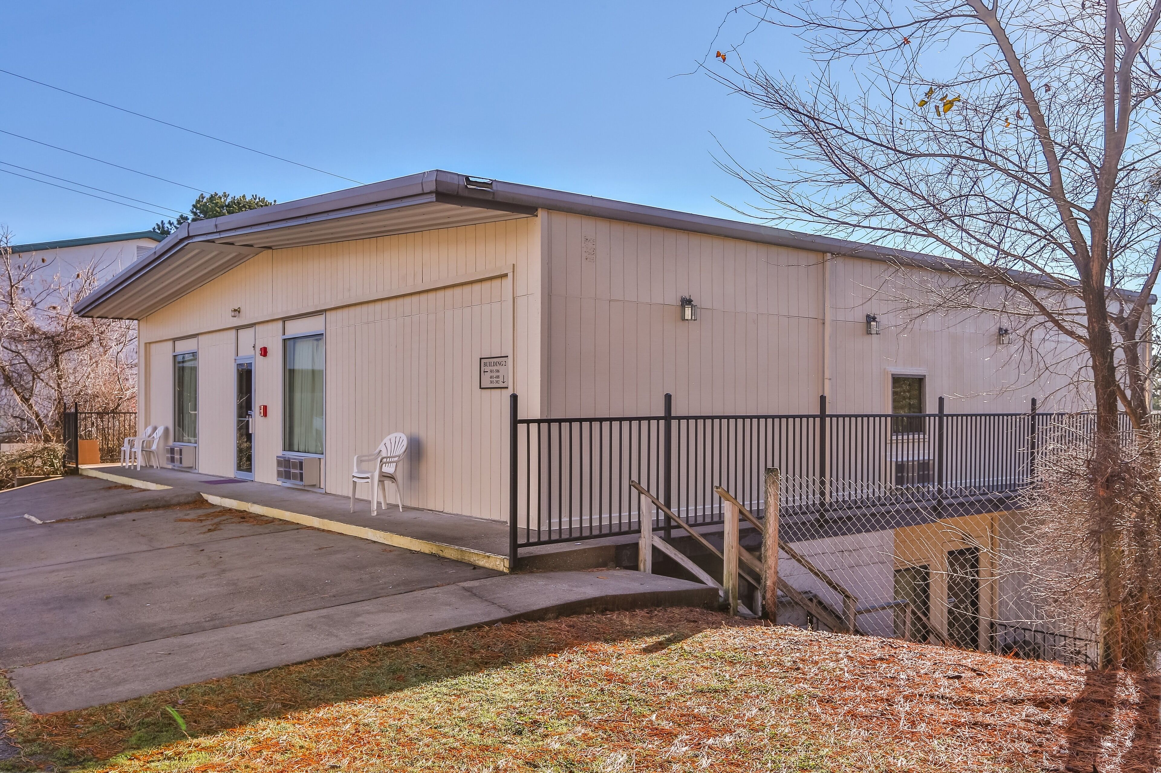 A building with a flat roof, a covered entrance, and a small outdoor seating area with chairs.