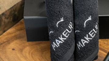 Duas toalhas pretas com a palavra 'MAKEUP' bordada, colocadas sobre uma superfície de madeira com uma caixa preta ao fundo.