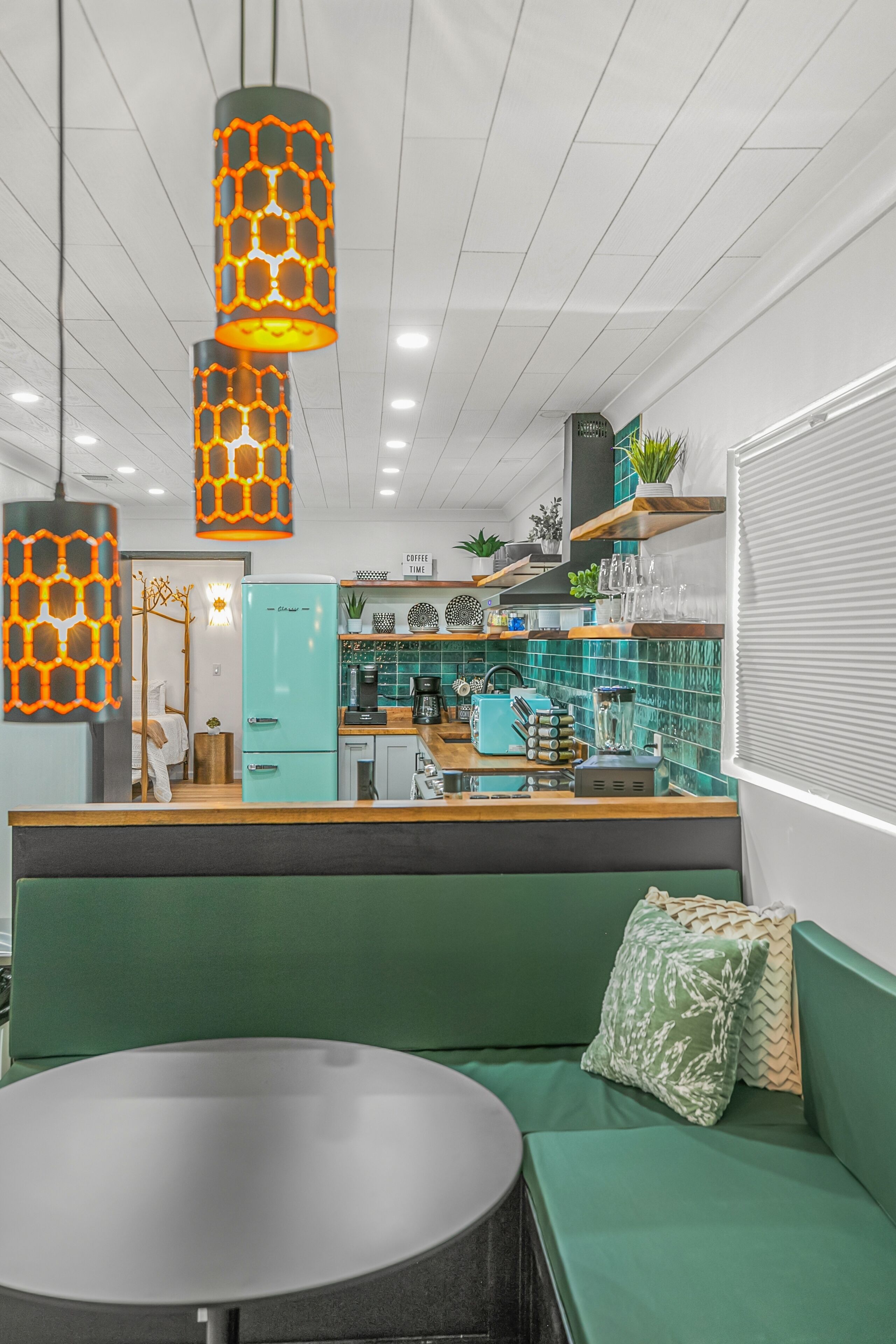 Une cuisine moderne avec un réfrigérateur de couleur turquoise, un comptoir en bois et des lampes orange suspendues.