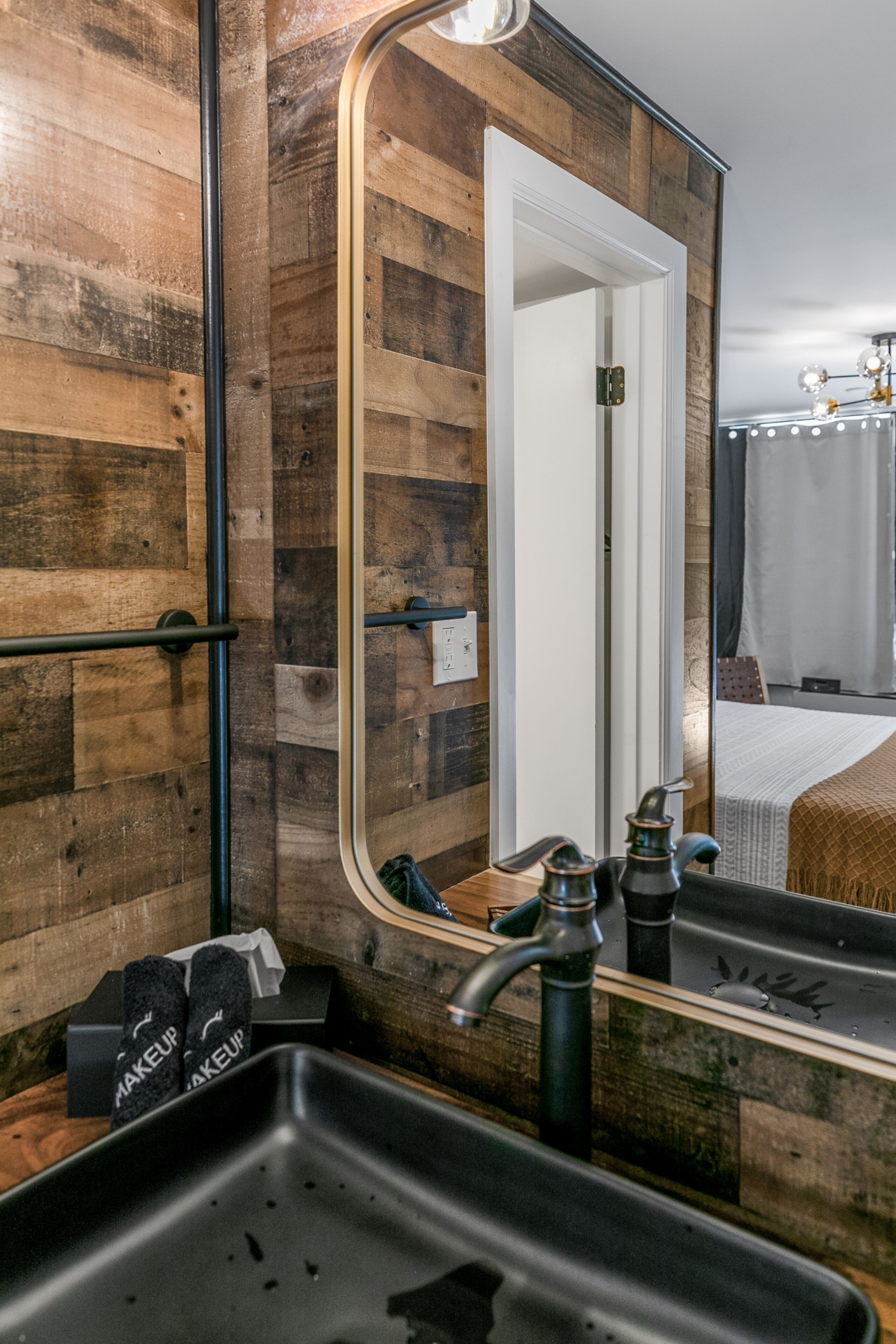 A bathroom with a wooden wall, a large mirror, a sink, and a towel rack.