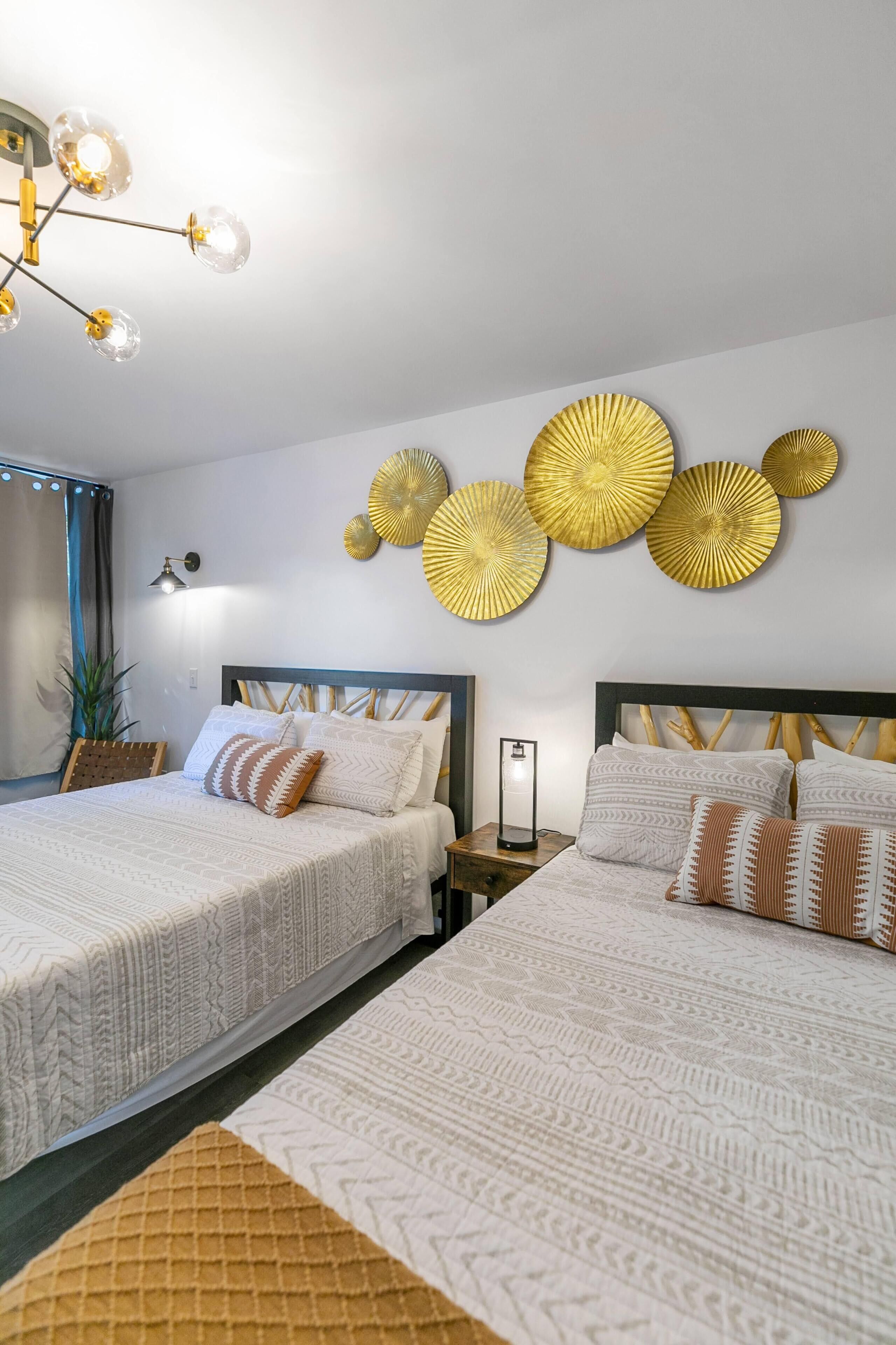 Una camera d'albergo con due letti, un lampadario, opere d'arte alle pareti e un comodino con una lampada.