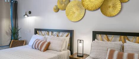 Una camera d'albergo con due letti, un lampadario, opere d'arte alle pareti e un comodino con una lampada.