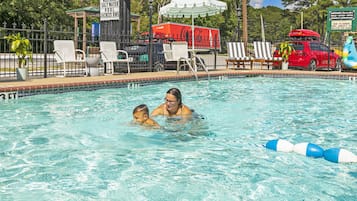 Uma piscina com uma fonte de água com a marca Coca-Cola, cadeiras de descanso e um caminhão Coca-Cola ao fundo.