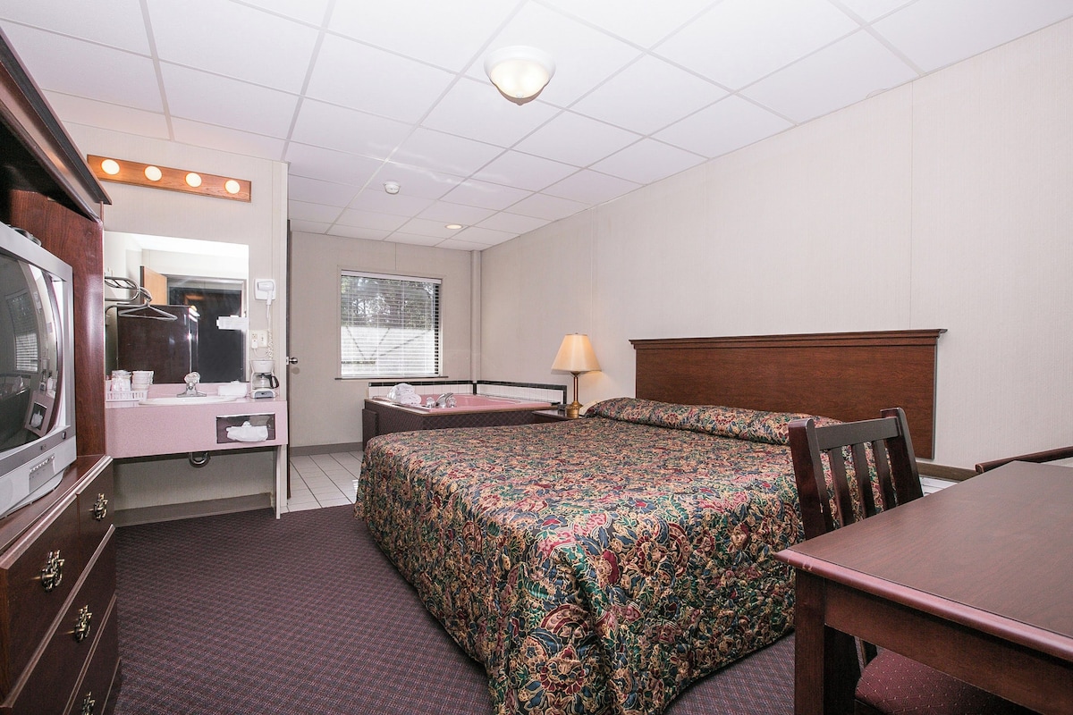 A hotel room with a bed, a desk, a chair, a TV, a mirror, and a window.