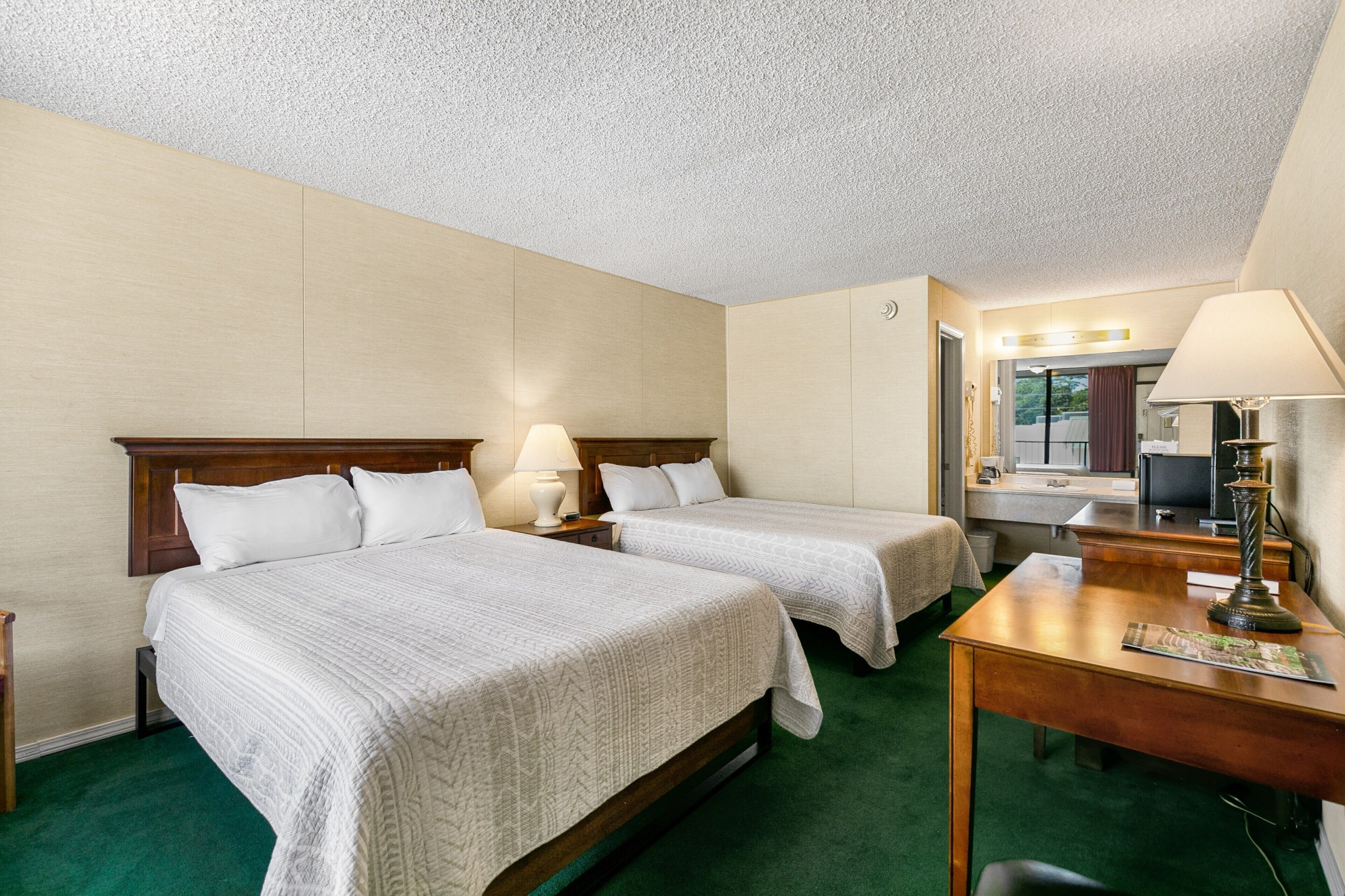 A hotel room with two beds, a desk, a chair, a lamp, and a mirror.