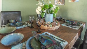 Una mesa de comedor servida con platos, tazones, vasos y un centro de mesa con flores.