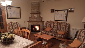 A cozy living room with a fireplace, patterned sofas, wooden furniture, and a dining table.