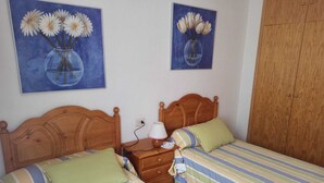 A bedroom with two beds, a wooden wardrobe, and two paintings of flowers on the wall.