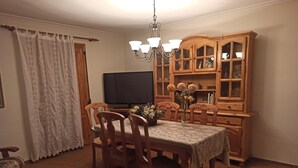A dining area with a wooden table and chairs, a chandelier, and a wooden cabinet with glass doors.