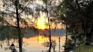 A wooden dock with a railing, an American flag, and a lamp post by a calm lake at sunset. - Suwannee Riverfront Retreat (Old Town)