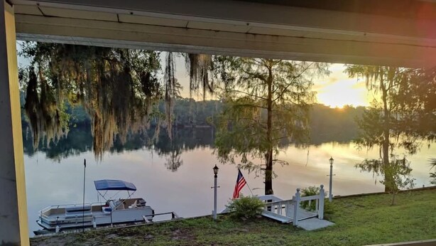 A serene lakeside view from a porch with a dock, a flag, and a lamp post. - Suwannee Riverfront Retreat (Old Town)