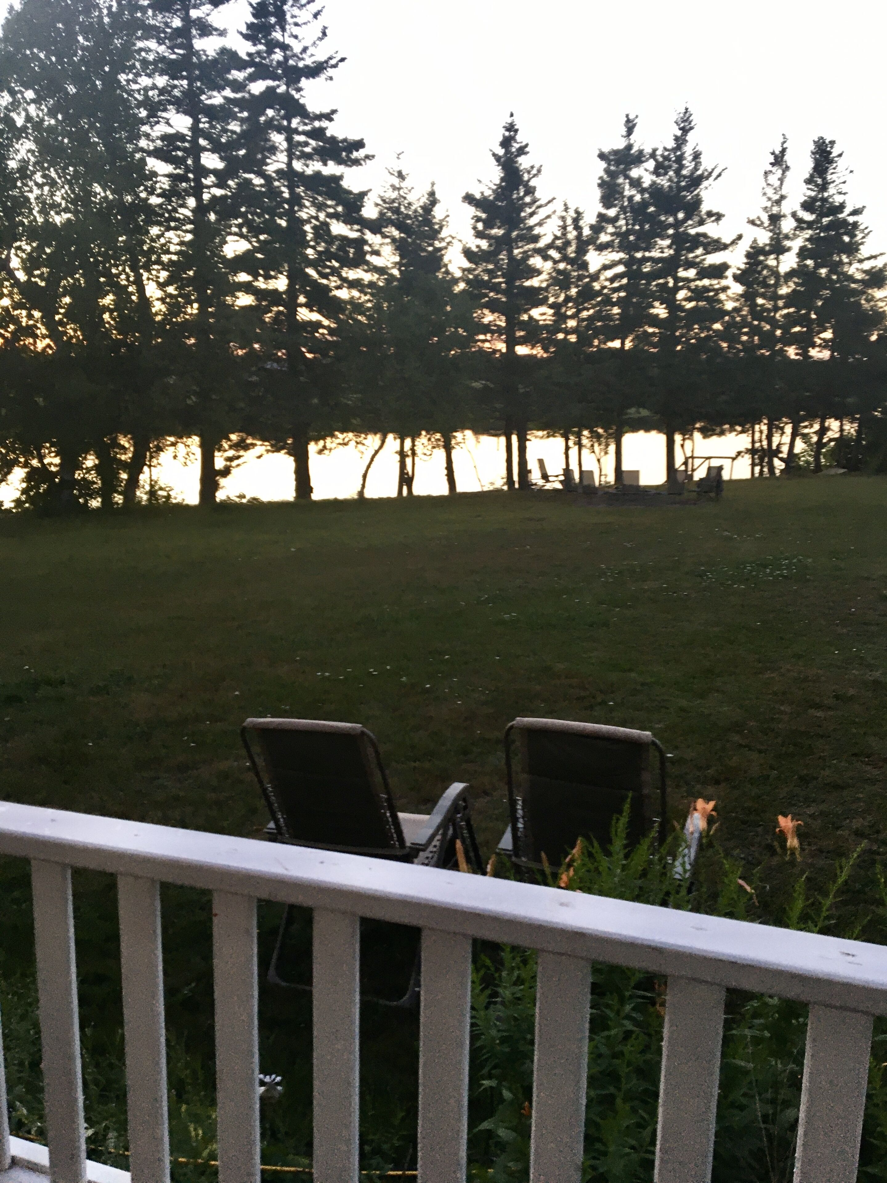 A deck with two chairs facing a grassy area with trees and a body of water in the background.