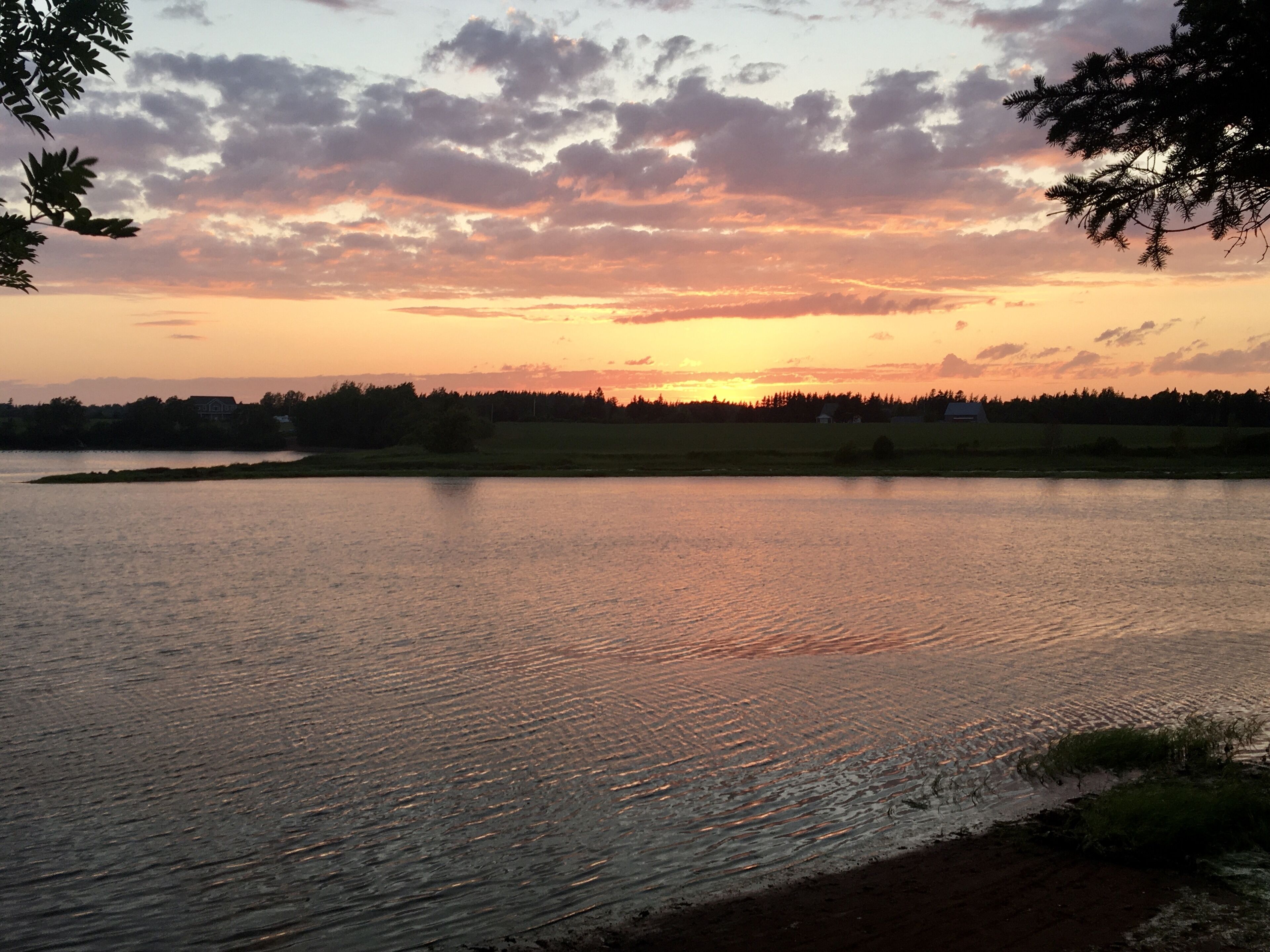 A lake with a sunset in the background, surrounded by trees and a distant shoreline.