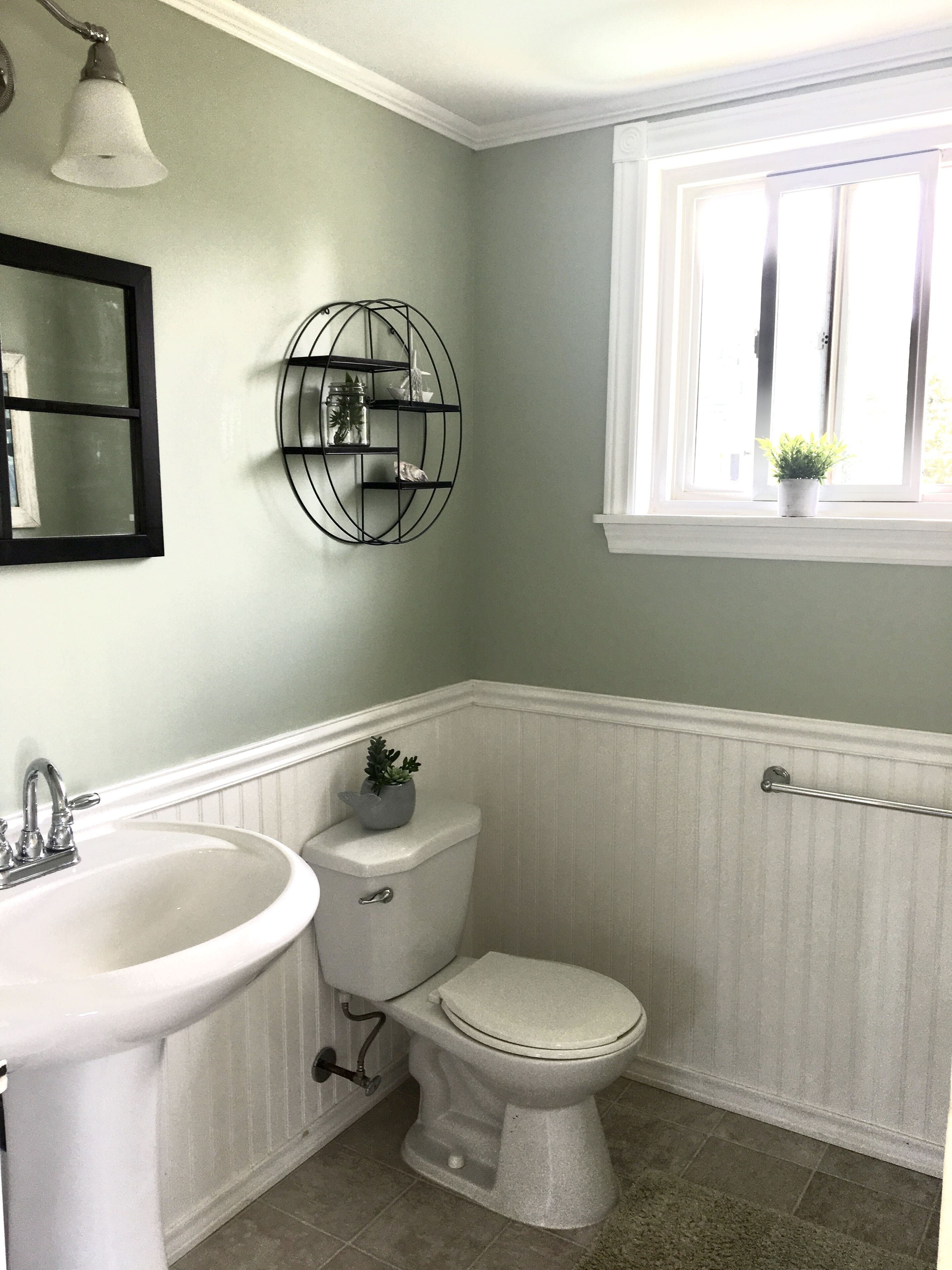 Un bagno con lavandino, water e mobile lavabo bianchi. Si vede del verde attraverso una finestra.