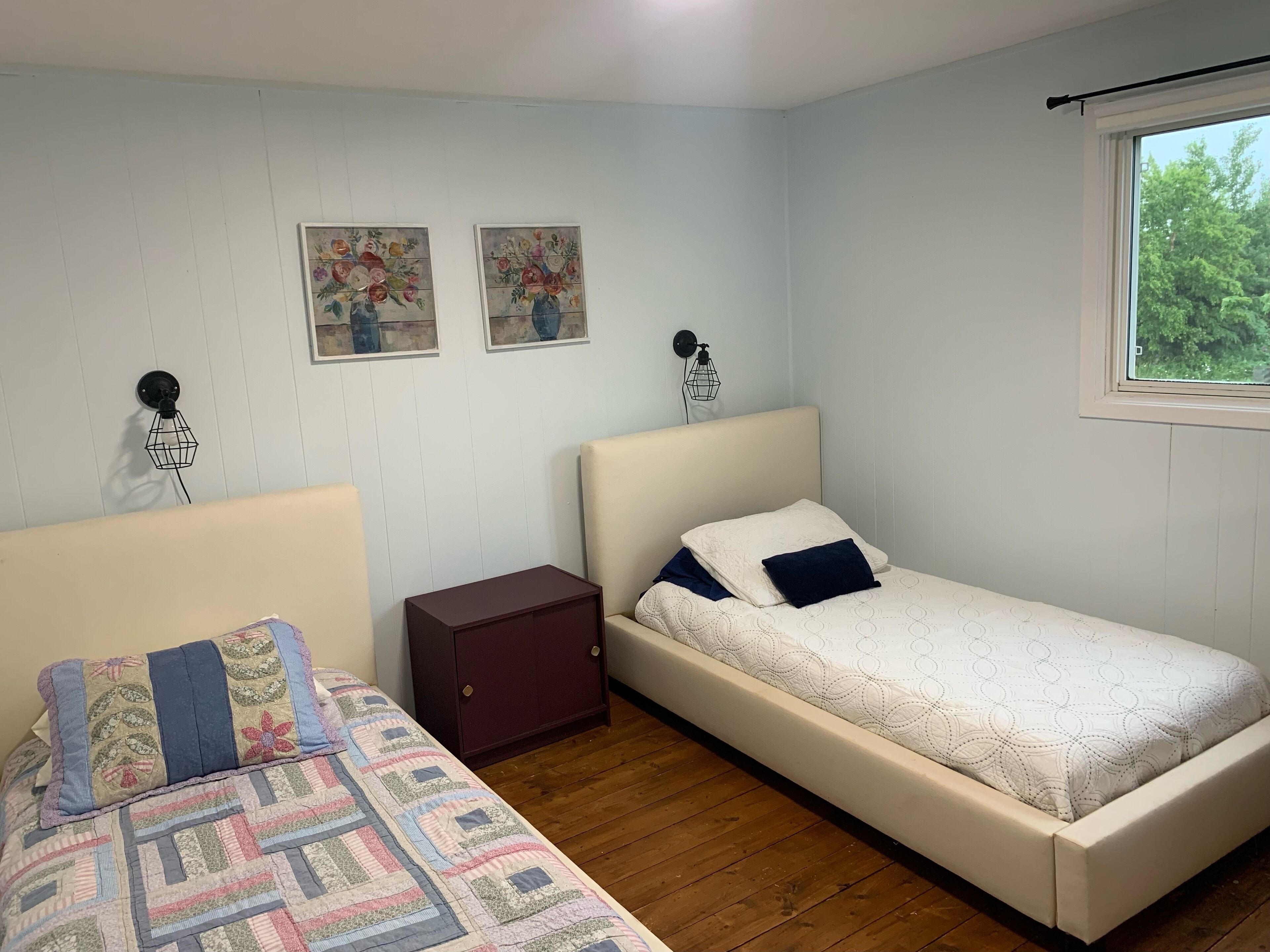 Une chambre avec deux lits, un plancher en bois, une fenêtre avec vue et deux œuvres d’art accrochées au mur.