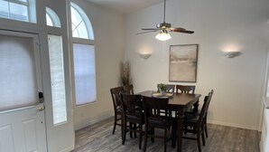 Uma sala de jantar com mesa e cadeiras de madeira, um ventilador de teto e um quadro na parede.