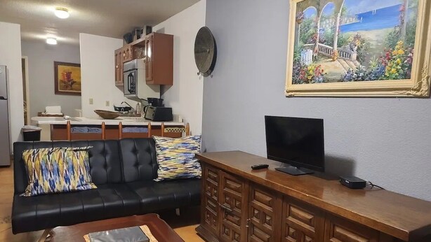 A living room with a sofa, coffee table, TV, wooden cabinet, and kitchen area in the background. - PRIVATE, COMFORTABLE & SPACIOUS! NEAR THE  MARINA, BEACHES & DOWNTOWN! CONDO 302 (San Felípe)