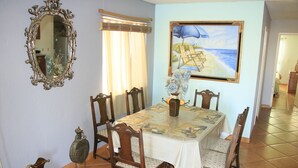 A dining area with a table set for six, surrounded by wooden chairs. A mirror hangs on the wall, and a beach-themed painting is above the table. - PRIVATE, COMFORTABLE & SPACIOUS! NEAR THE  MARINA, BEACHES & DOWNTOWN! CONDO 302 (San Felípe)