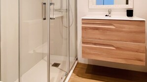 Un bagno moderno con doccia vetrata, mobile lavabo in legno e specchio con cornice decorativa.