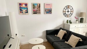 Un soggiorno con televisore, divano, due tavolini rotondi e opere d'arte che raffigurano Hawaii, L'Avana e Barcellona.