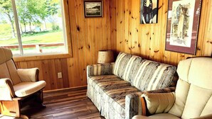 A wooden-paneled room with a sofa and two armchairs, a window, and framed artwork on the walls. - Comfy St Lawrence getaway for  Fisher or birdwatcher or for a family vacation  (Saint-Anicet)