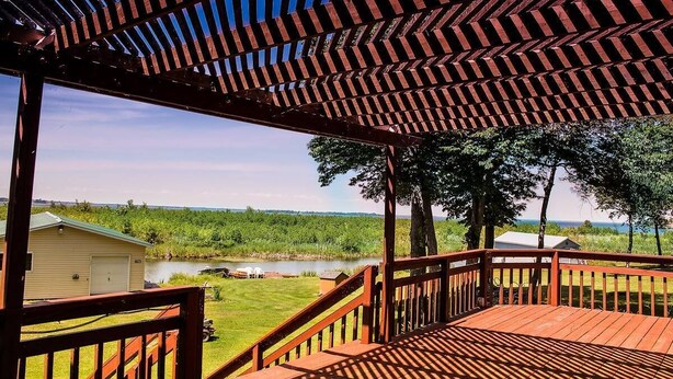 A wooden deck with a view of a lake and a grassy area. - Comfy St Lawrence getaway for  Fisher or birdwatcher or for a family vacation  (Saint-Anicet)