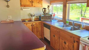 A kitchen with wooden cabinets, a stainless steel sink, and a window with a view of greenery outside. - Comfy St Lawrence getaway for  Fisher or birdwatcher or for a family vacation  (Saint-Anicet)