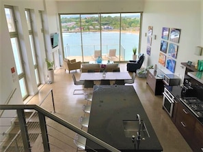 A modern kitchen with a large island, dining area with chairs, and a view of a beach through large windows. - Stunning Oceanfront Home @ Kalapaki Bay, AC, Sleeps 8 (Lihue)