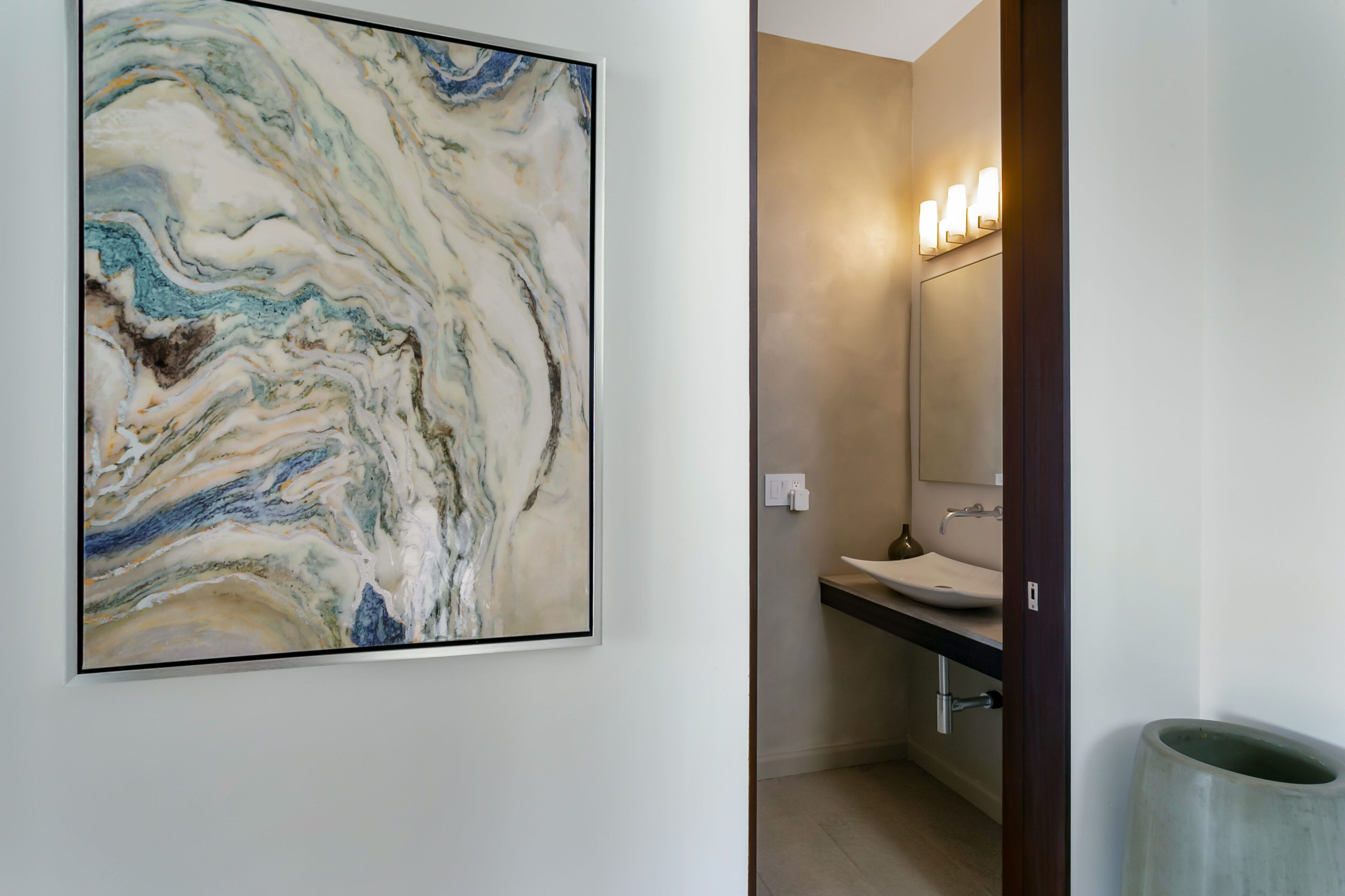 Un baño con una obra de arte de mármol en la pared, un lavabo y un espejo con luces.